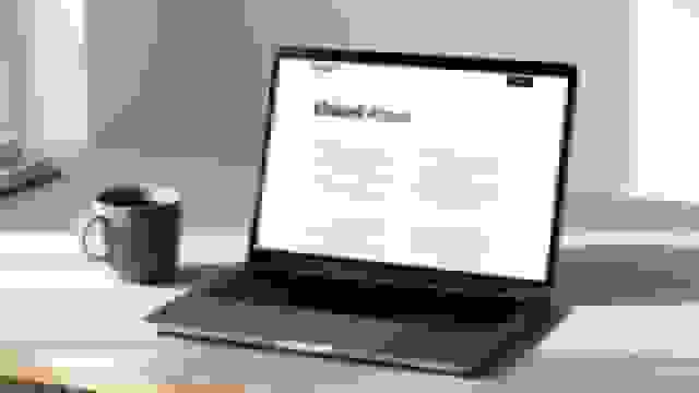 A laptop on a desk displaying a 'Linked About' page, with a coffee mug and books.