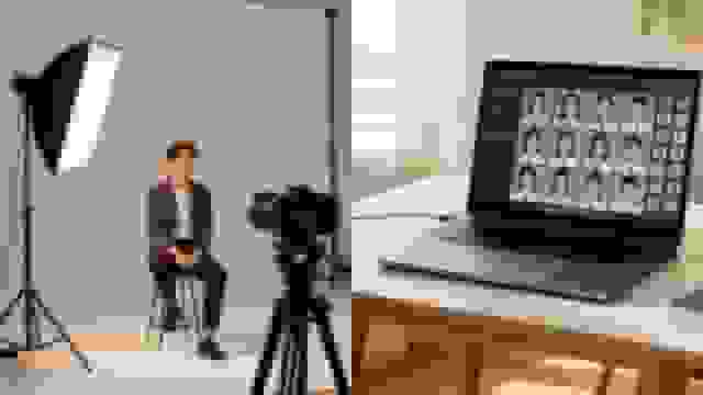 A young man posing for a headshot in a studio, alongside a laptop displaying professional ID photos.