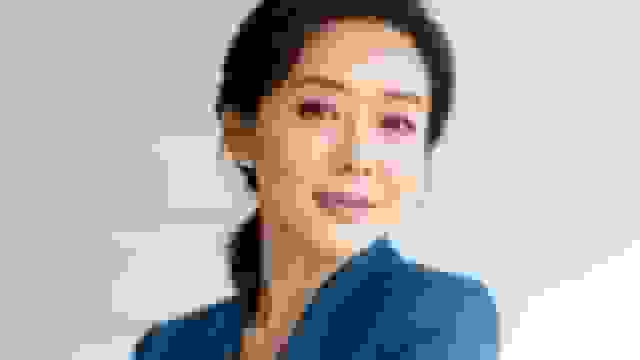 Close-up of a smiling Asian woman in a blue blazer looking confidently at the camera.